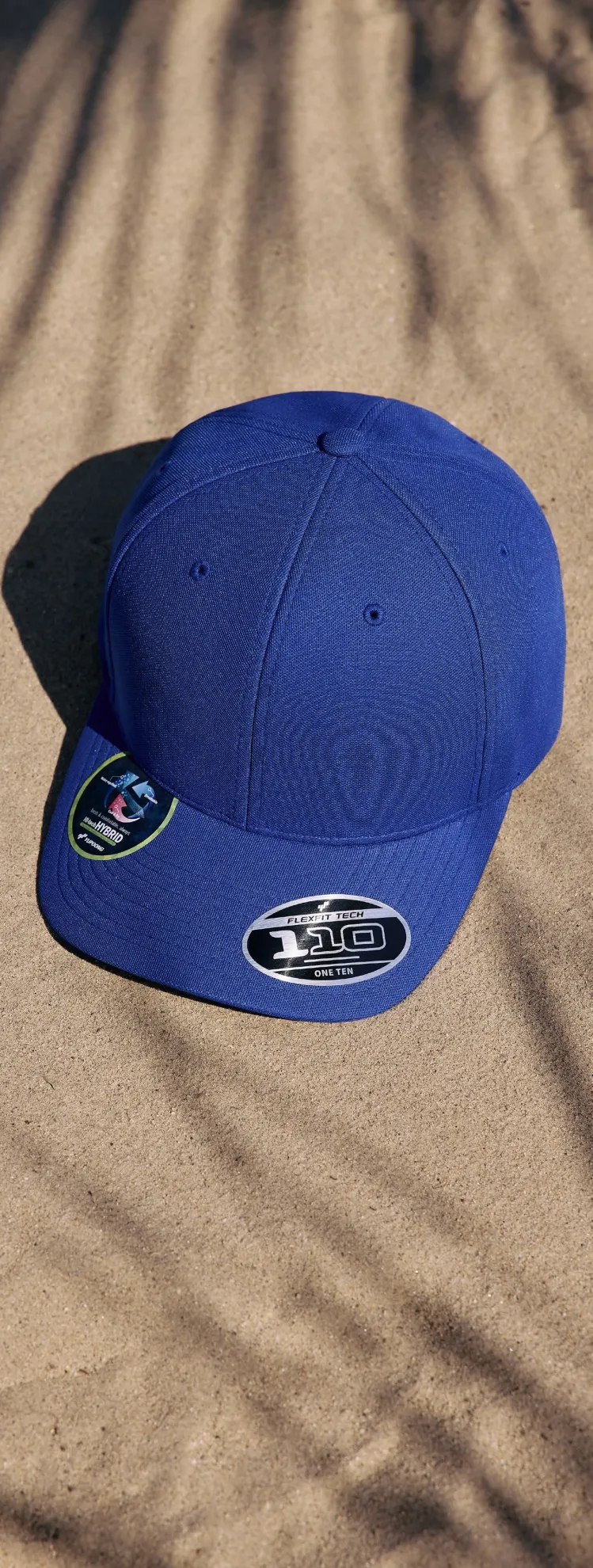 Gorra Flexfit 110 azul royal sobre la arena con sombras de palmera