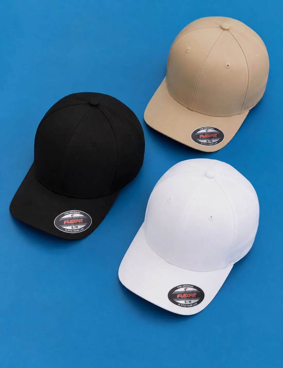 Tres gorras Flexfit Original en negro, caqui y blanco sobre fondo azul