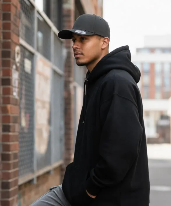 Hombre con sudadera negra y gorra snapback negra en una calle de ladrillo