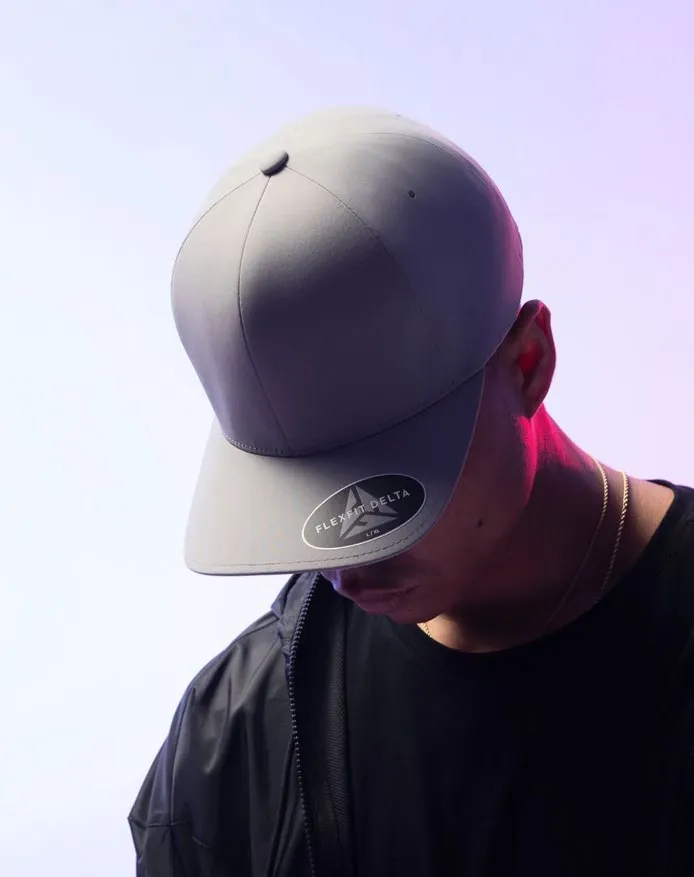 Hombre con gorra Flexfit Delta gris claro y la cabeza inclinada sobre fondo lila